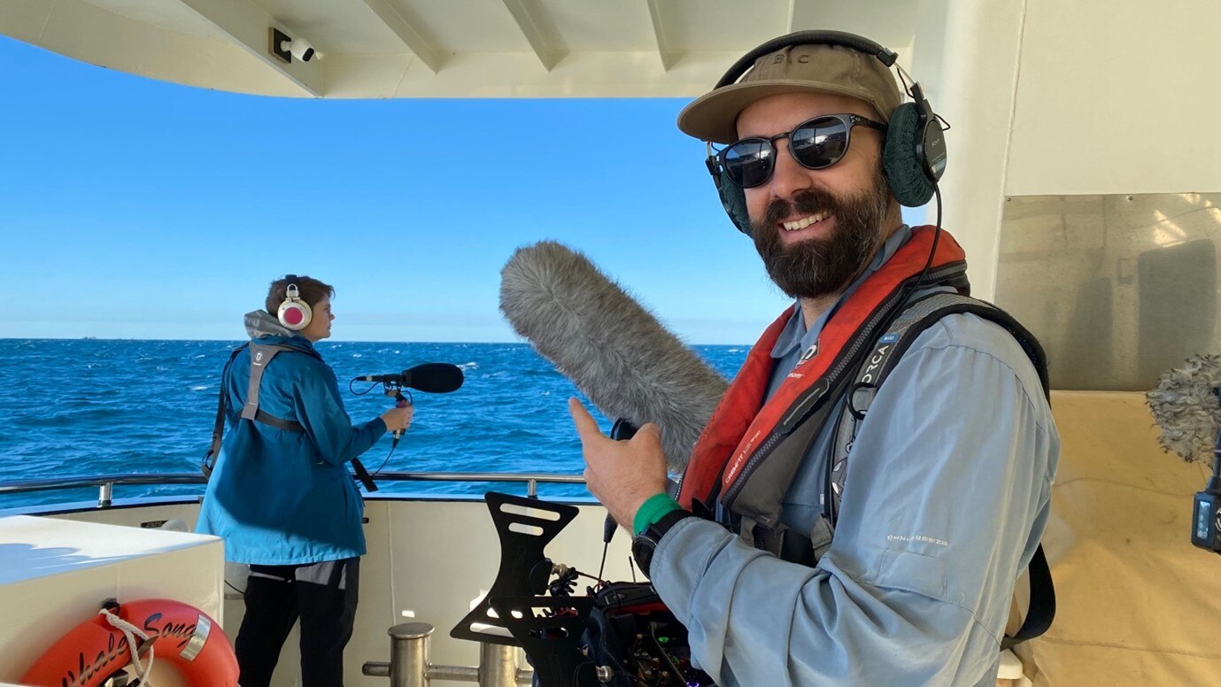 Man with headphones on and microphone on a boat.