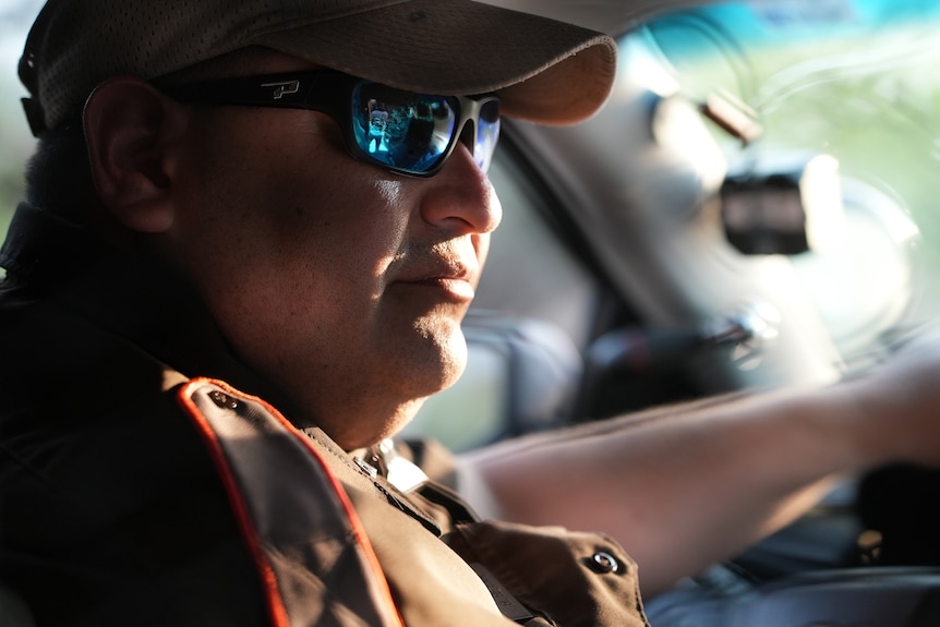 A man wearing a cap and sunglasses in a car.