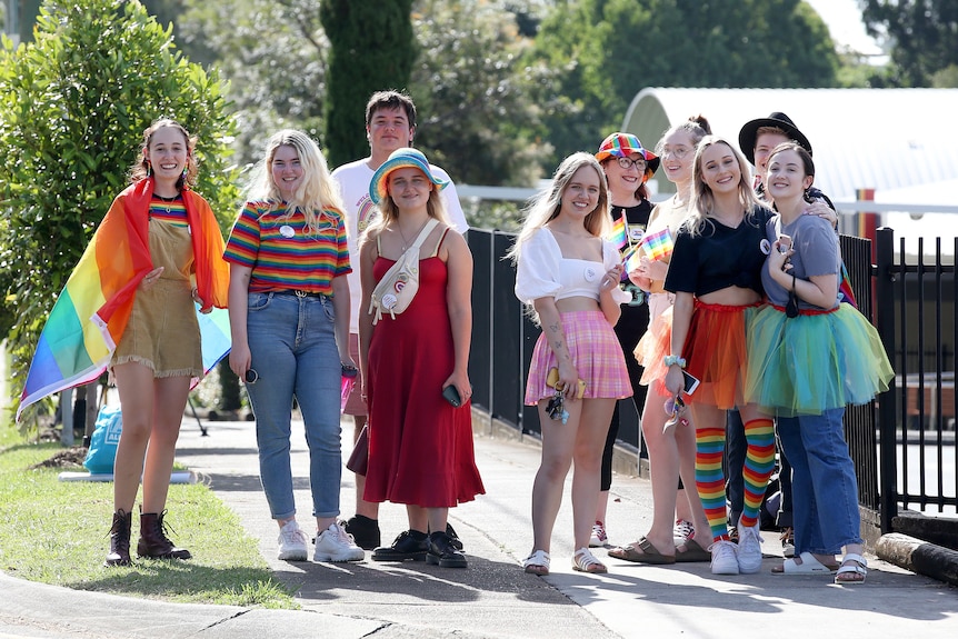 A group of young people in flamboyant rainbow outfits stand outside Citipointe Christian College.