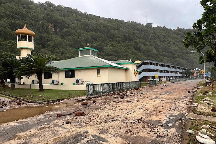 A road in front of large buildings near the waterfront on Christmas Island, covered in sand and debris from large waves.