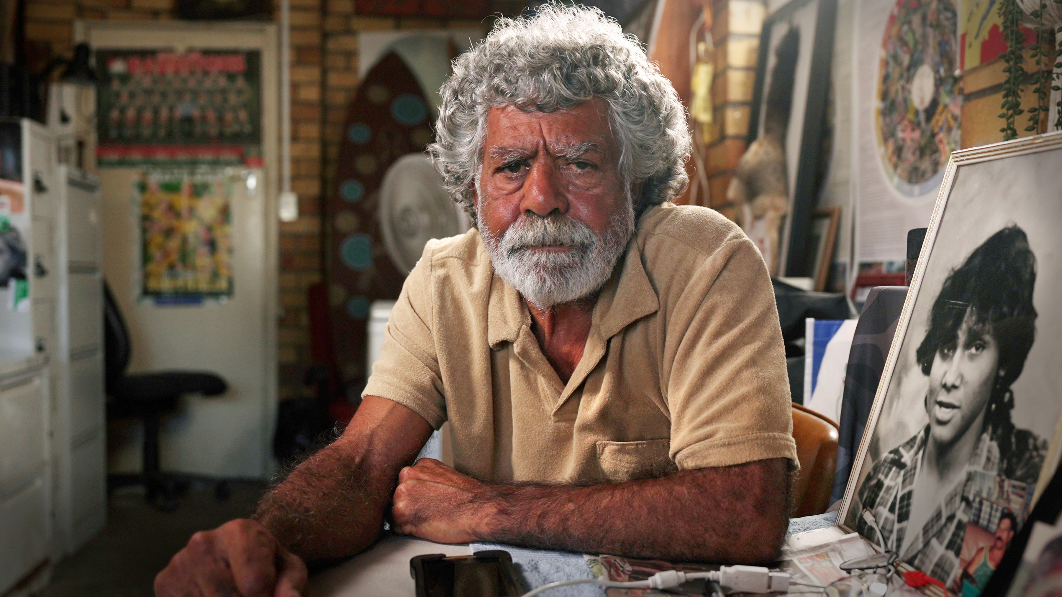 A man sits at a table with a furrowed brow, to his left a photo of a young teen