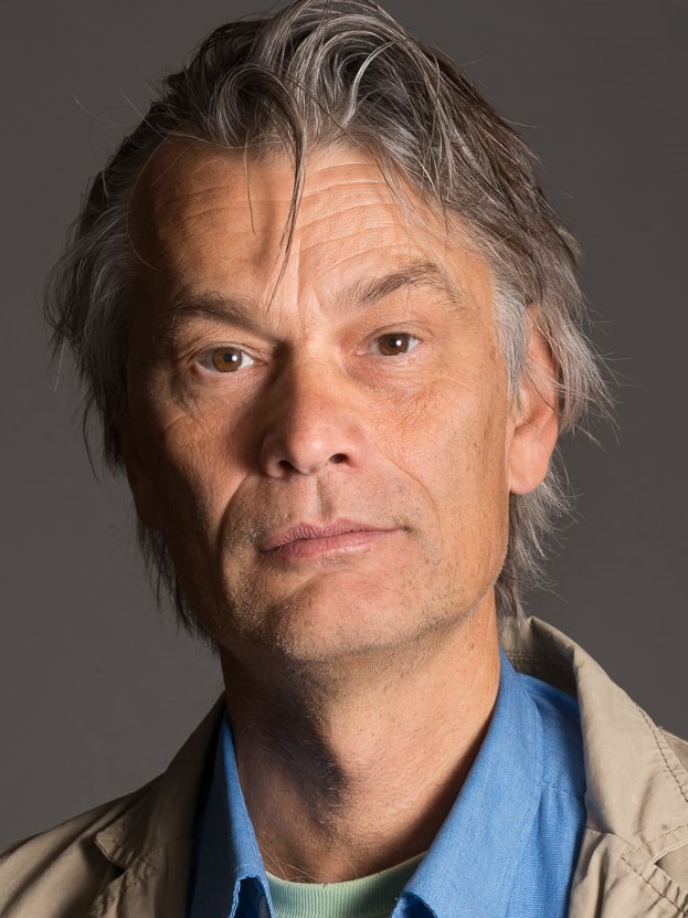 A photo portrait of a man in a blue shirt and a light brown jacket.