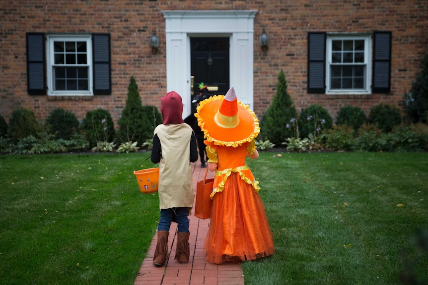 Two children in Halloween costumes walking towards a house