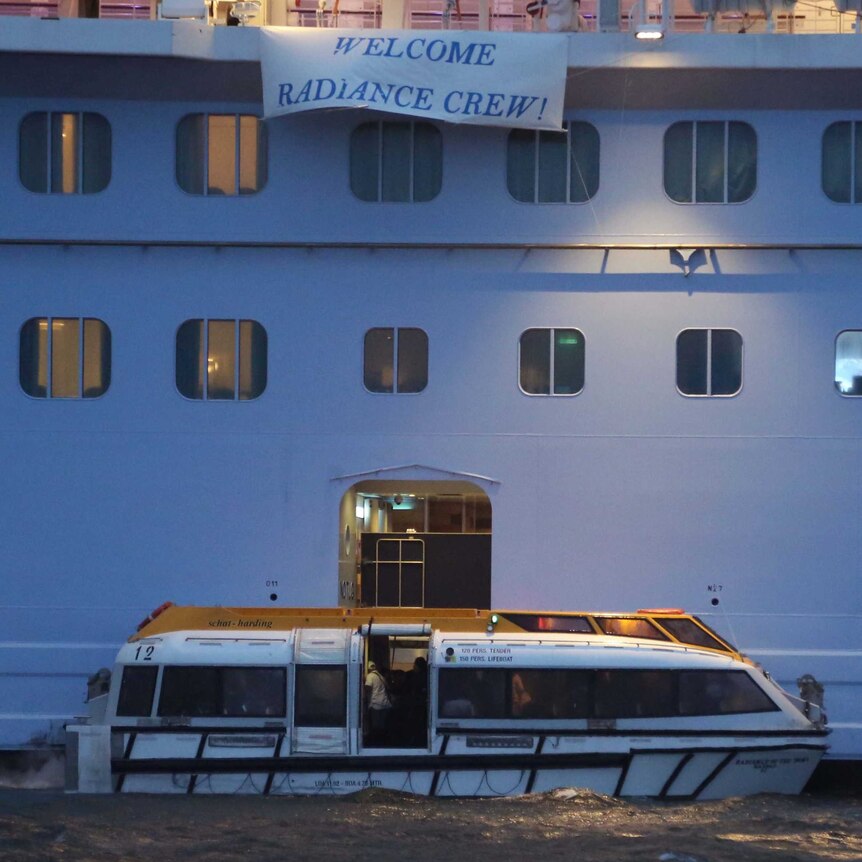 A tender boat sits alongside a cruise ship with a banner reading 'Welcome Radiance Crew!'
