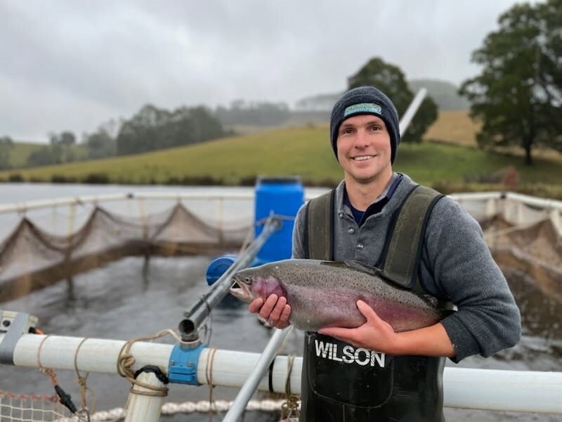 A man standing in front of a tank holding a good sized trout