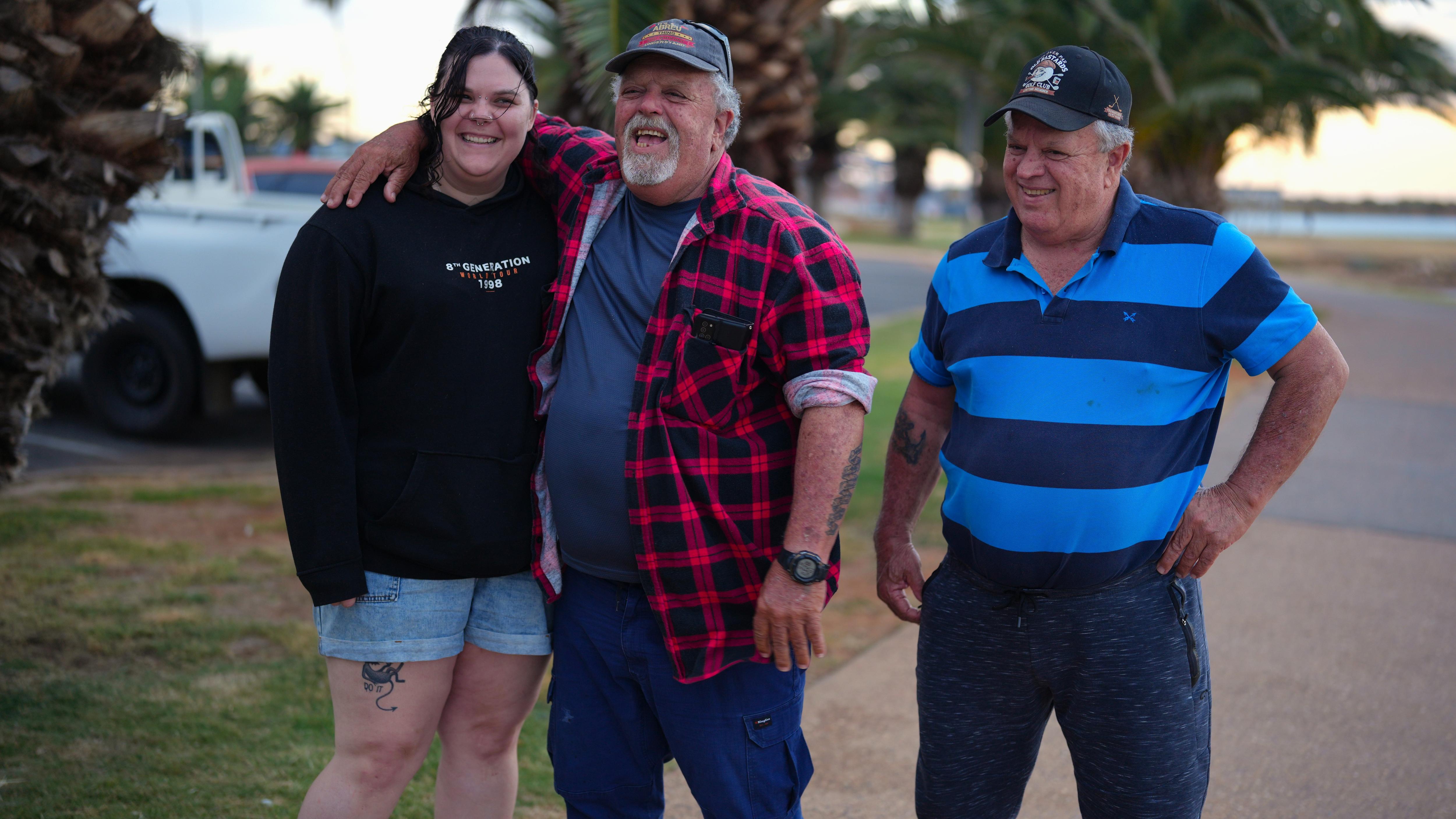 A man standing in the middle with his brother on his right and his arms on his daughter's shoulder on his left.