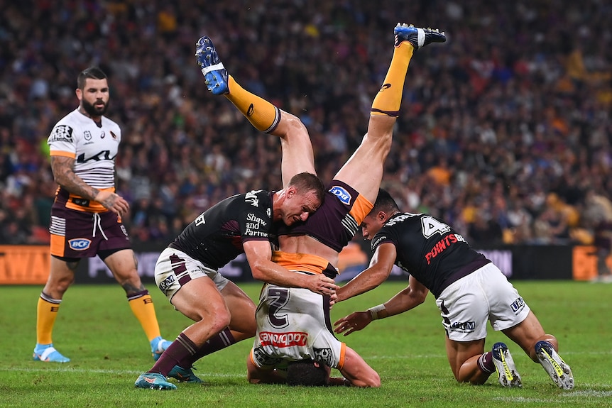 Daly Cherry-Evans and another Manly player grab Corey Oates, who is upside down during an NRL game.