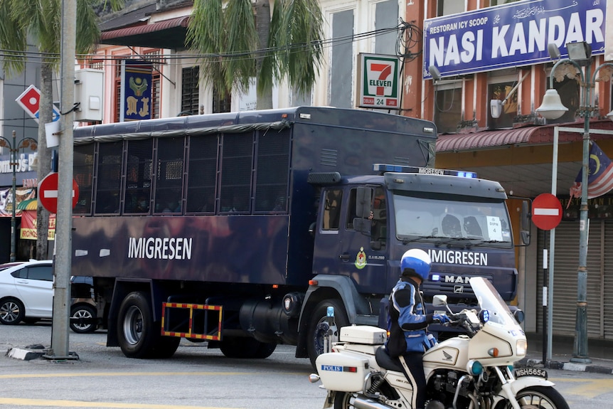 A police motorbike rides alongside a Malaysian immigration truck carrying migrants