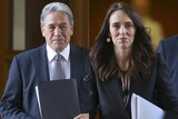 Jacinda Ardern walks with Winston Peters, both clutching papers and staring ahead.