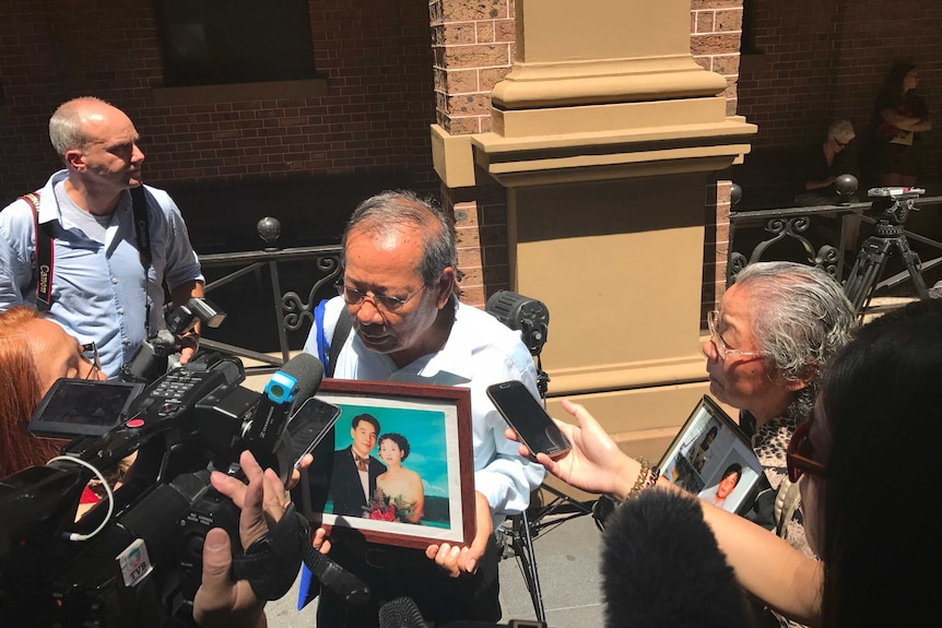 Yang Fei Lin and Feng Qing Zhu, who are holding pictures of the murdered members of the Lin Family, are surrounded by the media.