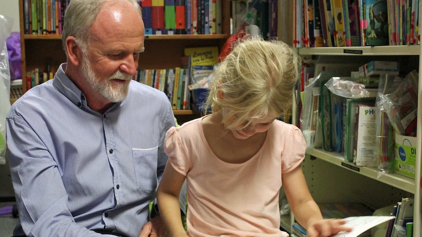 Trinity, whose grandmother is a volunteer at the Pyjama Foundation, reads a picture book with the foundation's Kevin Gallard.