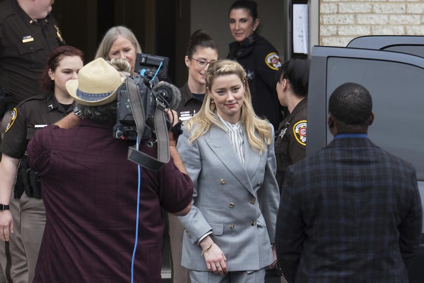 A photo of Amber Heard departing the Fairfax County Courthouse with police and reporters around her. 