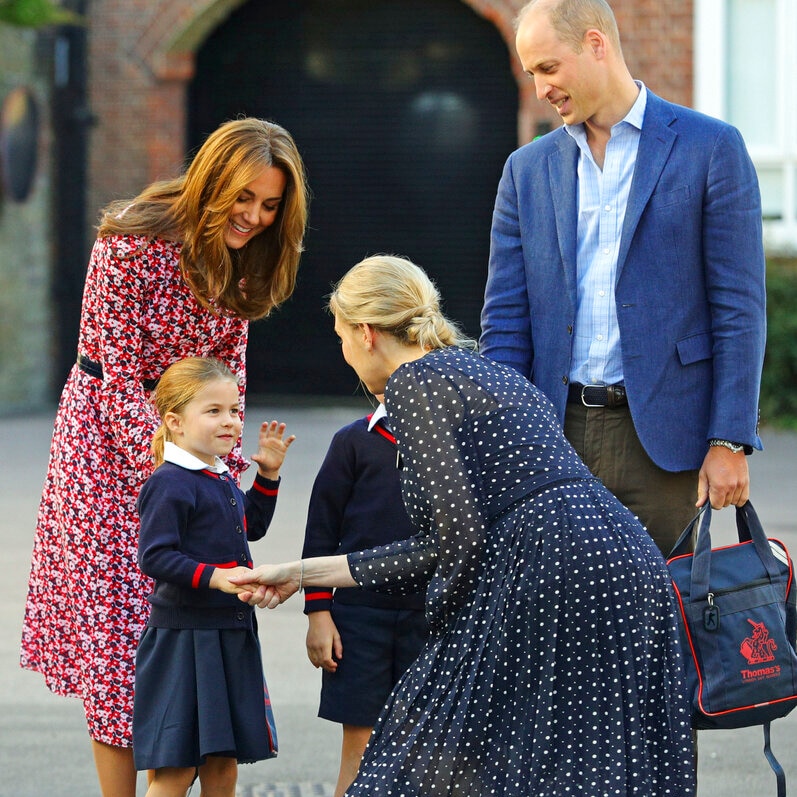 A woman curtseys as she shake's Princess Charlotte who is flanked by her brother and parents.