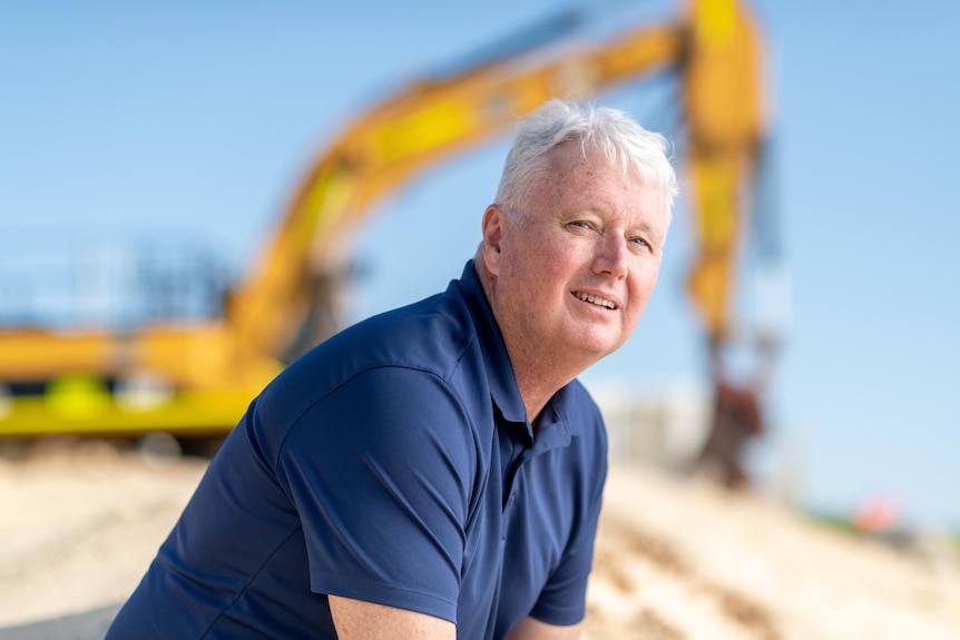 A man sits on the beach in front of digging equipment.