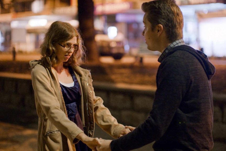 A you woman is holding hands with a young man on a street at night