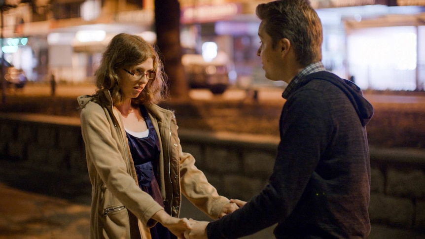 A you woman is holding hands with a young man on a street at night