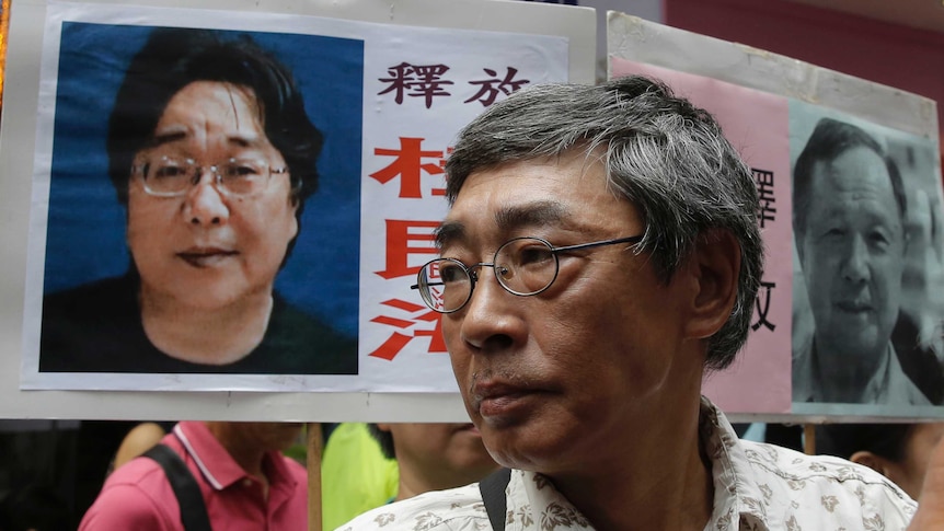 Tight shot of a man standing in front of a placard with two male faces on it.