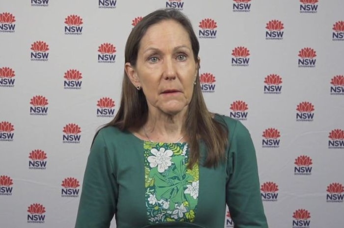 A woman with brown hair and a green shirt against a NSW Government backdrop