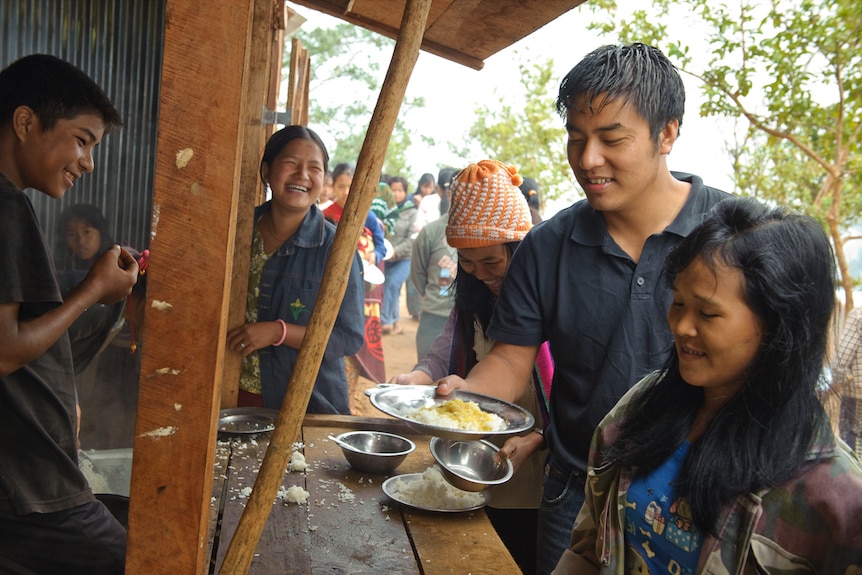 A smiling Asian man holds a dish of food in a marketplace