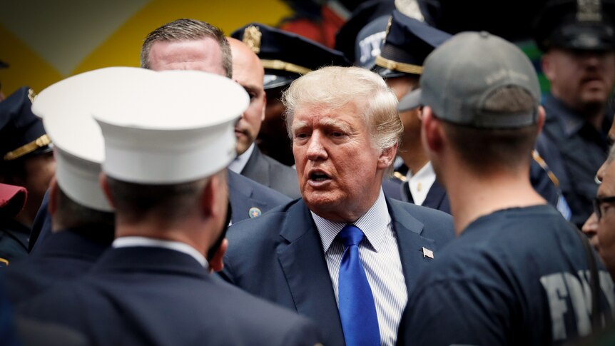 Donald Trump in a bright blue tie talking to a group of police officers and firemen in dress uniforms 