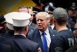 Donald Trump in a bright blue tie talking to a group of police officers and firemen in dress uniforms 