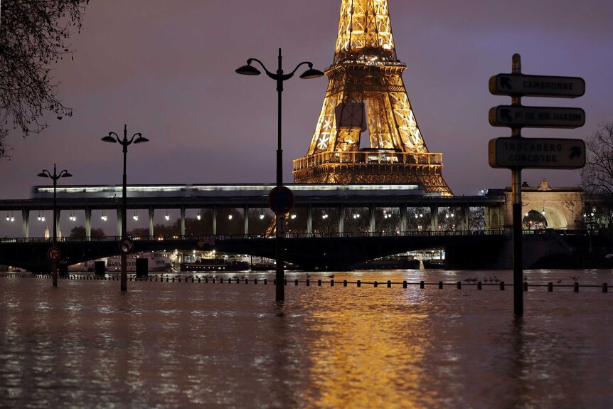 A photo taken at night time shows the Eiffel Tower lit up and surrounded by floodwaters