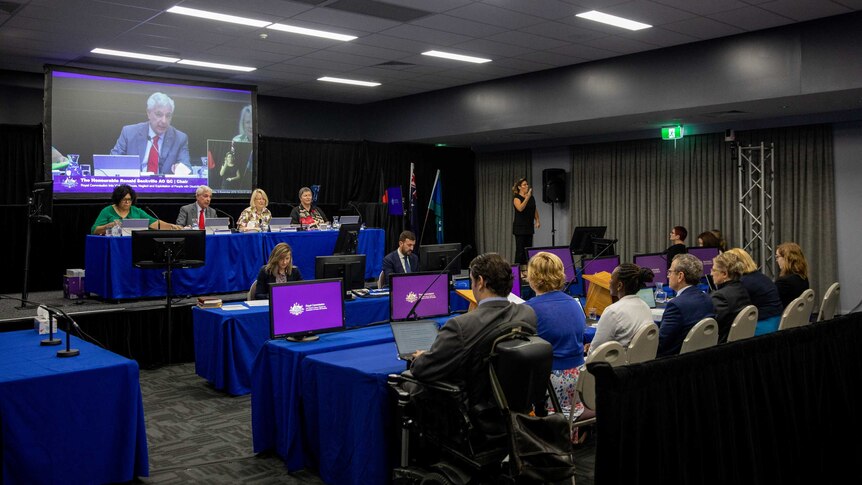 A wide shot shows inside the public hearing in Townsville led by Ronald Sackville.