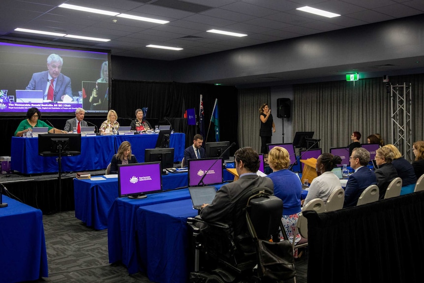 A wide shot shows inside the public hearing in Townsville led by Ronald Sackville.