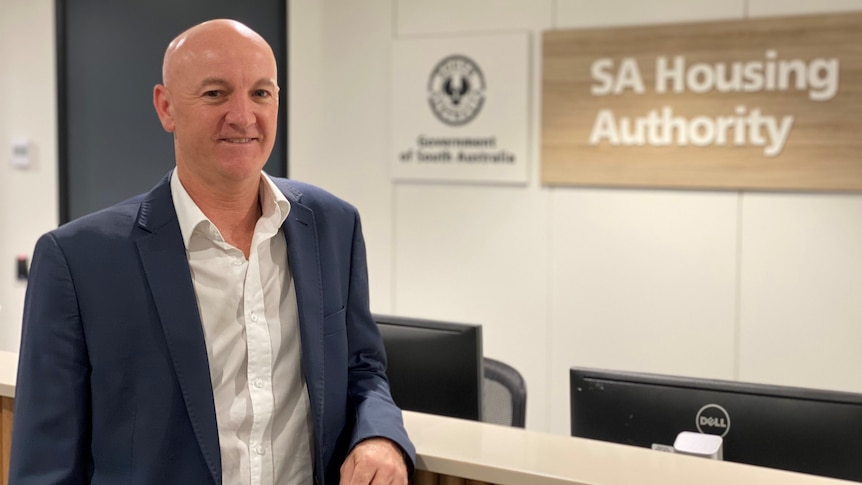 A man leans on a counter smiling in front of a South Australian government sign