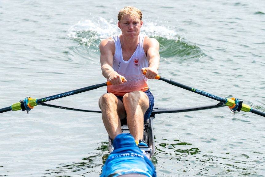 a man rowing in a netherlands team kit. he looks like he is exerting himself 