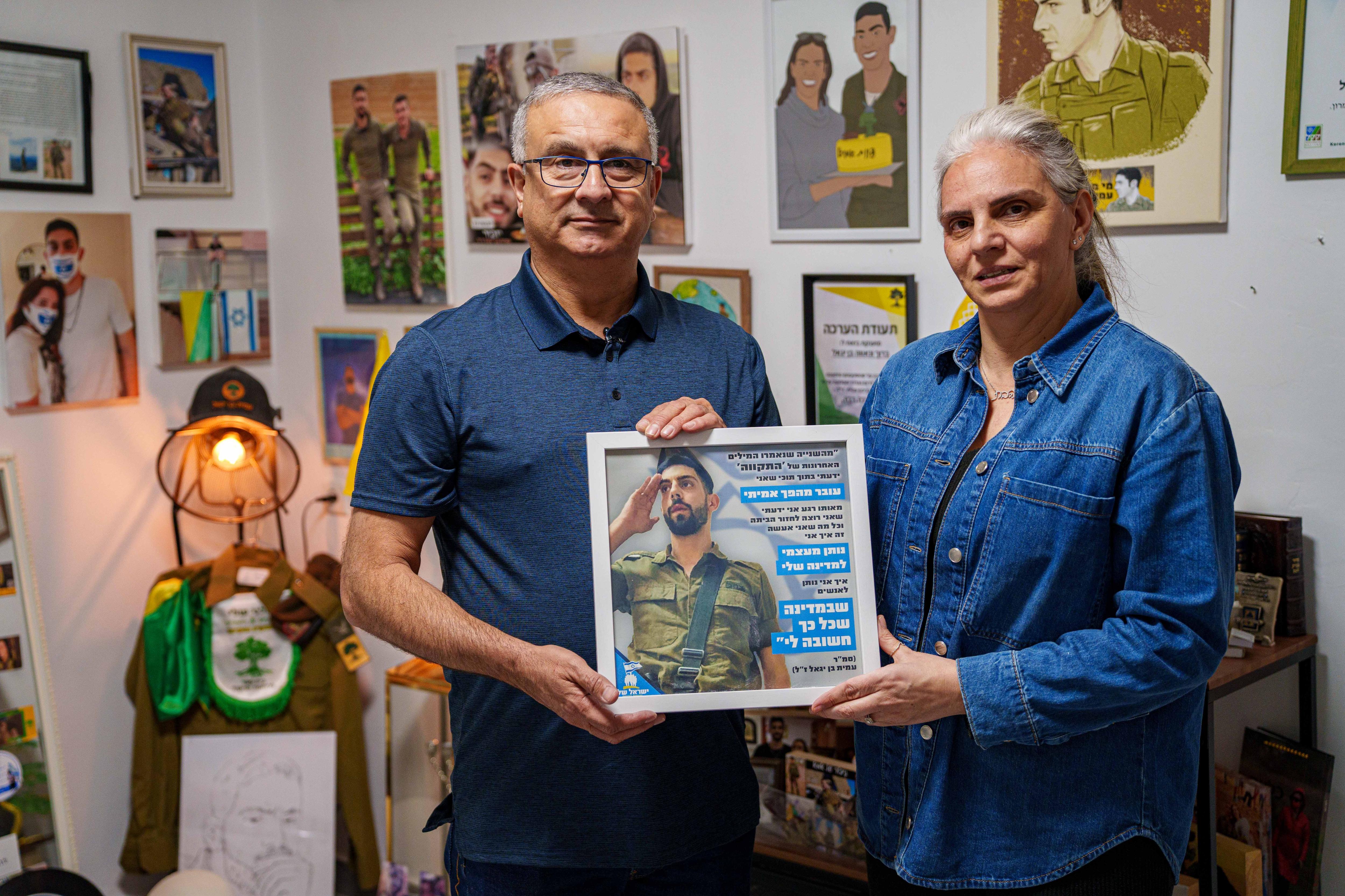 A man and a woman holding a portrait of their son in his bedroom.