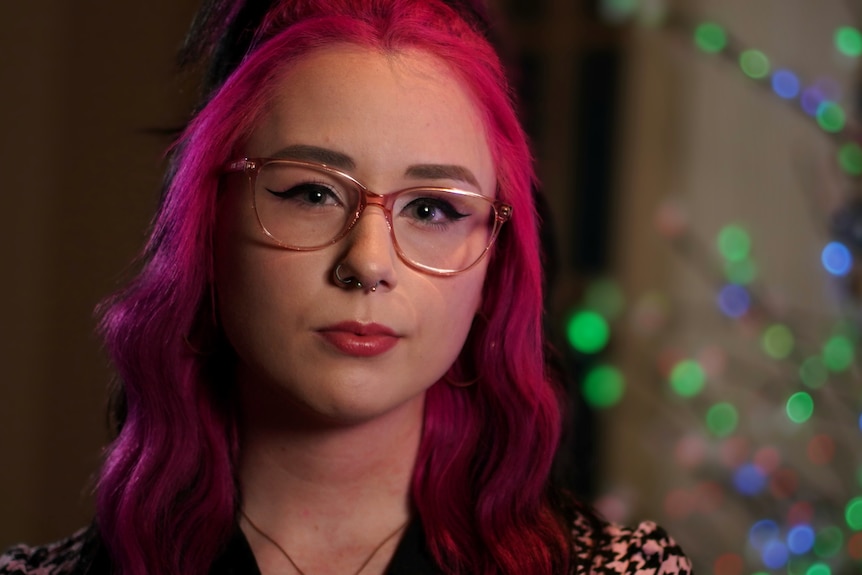 Raven wearing glasses with pink hair looking serious.