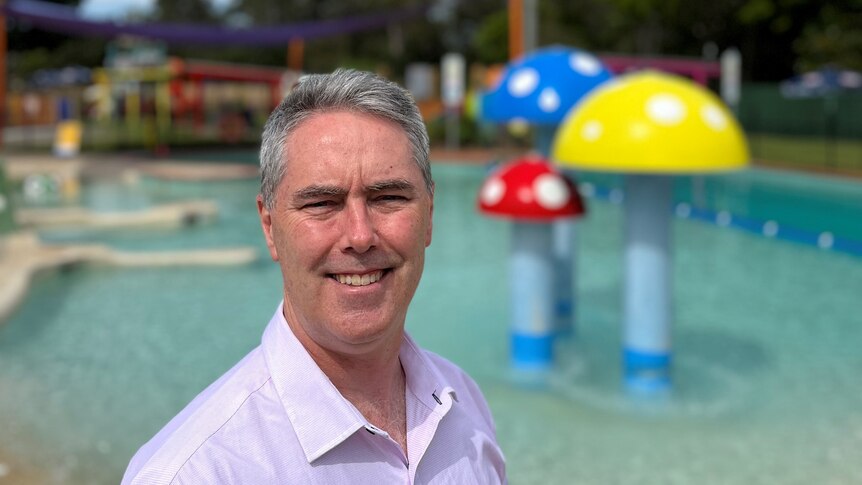 A man with grey hair and a white shirt smiling in front of a pool.
