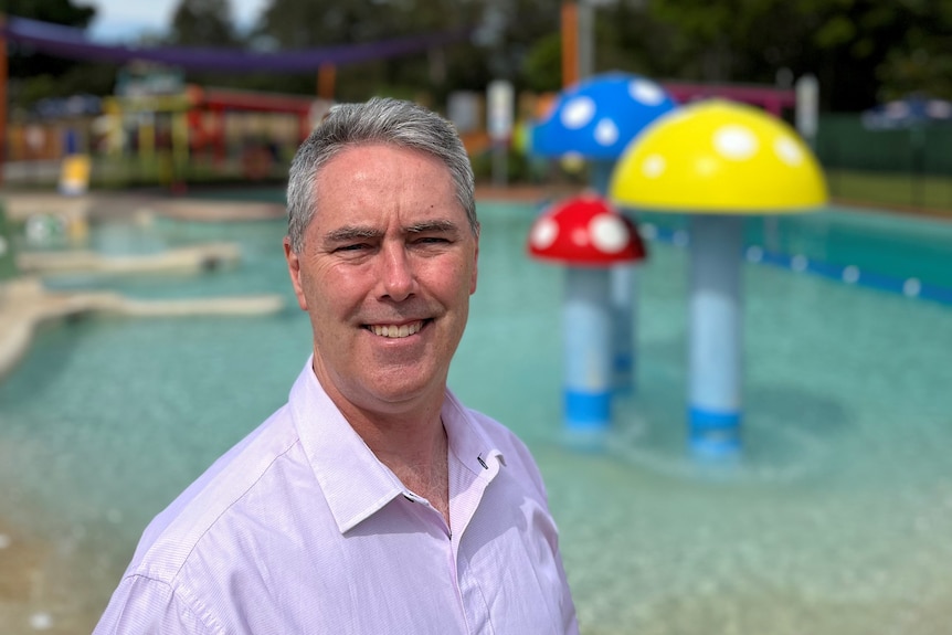 A man with grey hair and a white shirt smiling in front of a pool. 