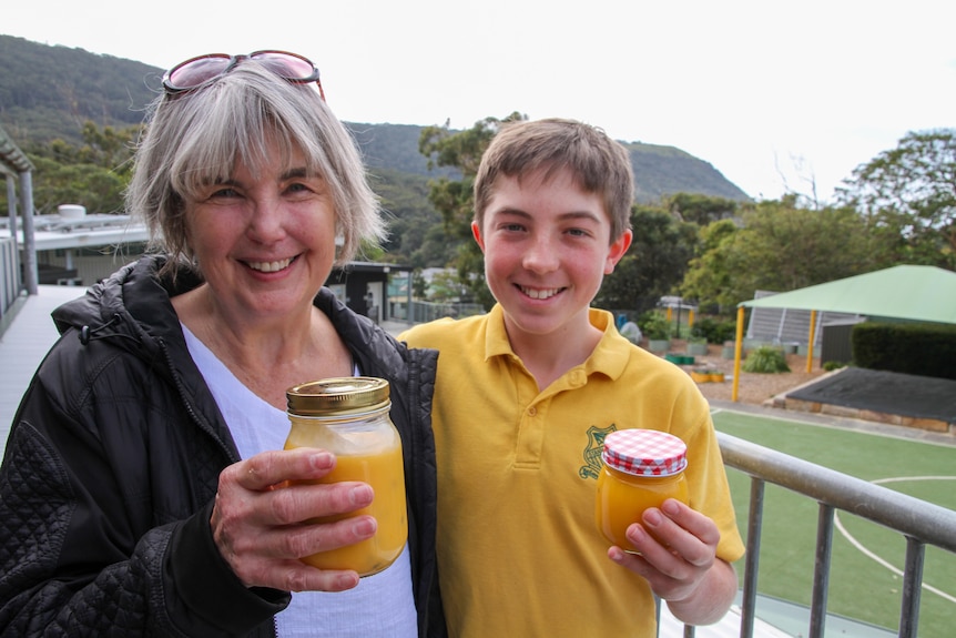 An older woman stands with her grandson holding jars of lemon curd.