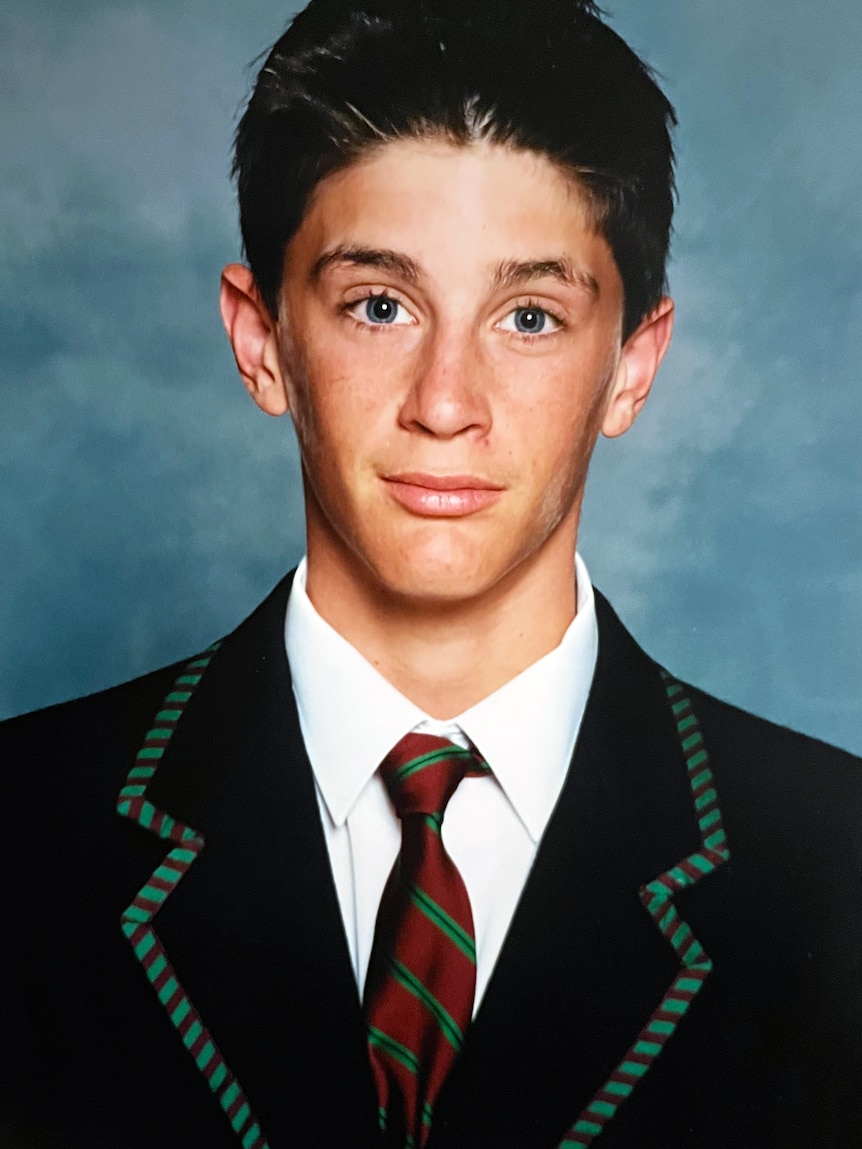 A school portrait photo of a teenage boy wearing a dark blazer and a maroon and green striped tie.