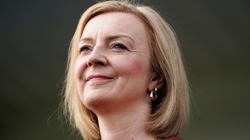 Liz Truss, with blonde hair and gold earrings, grins as she looks into the distance.