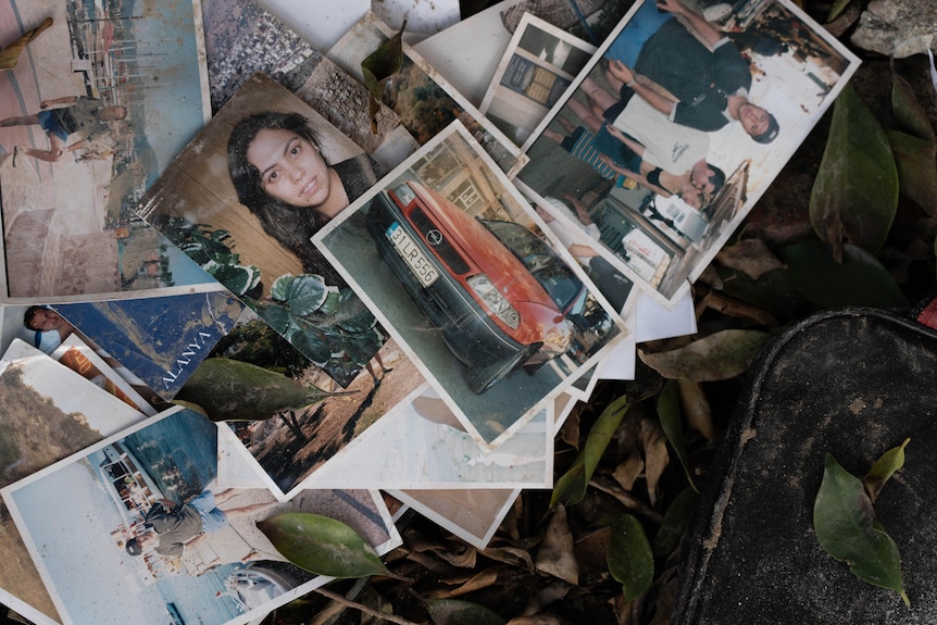 A pile of home photographs showing an unknown woman and family lay abandoned on the ground near a destroyed residential building