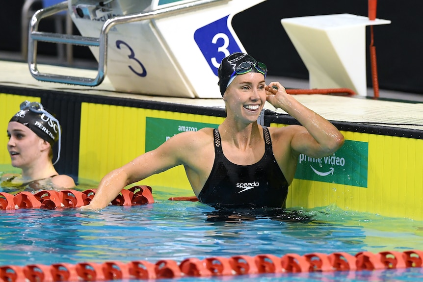 Una mujer en un traje de baño atlético sonríe desde el final de la piscina.