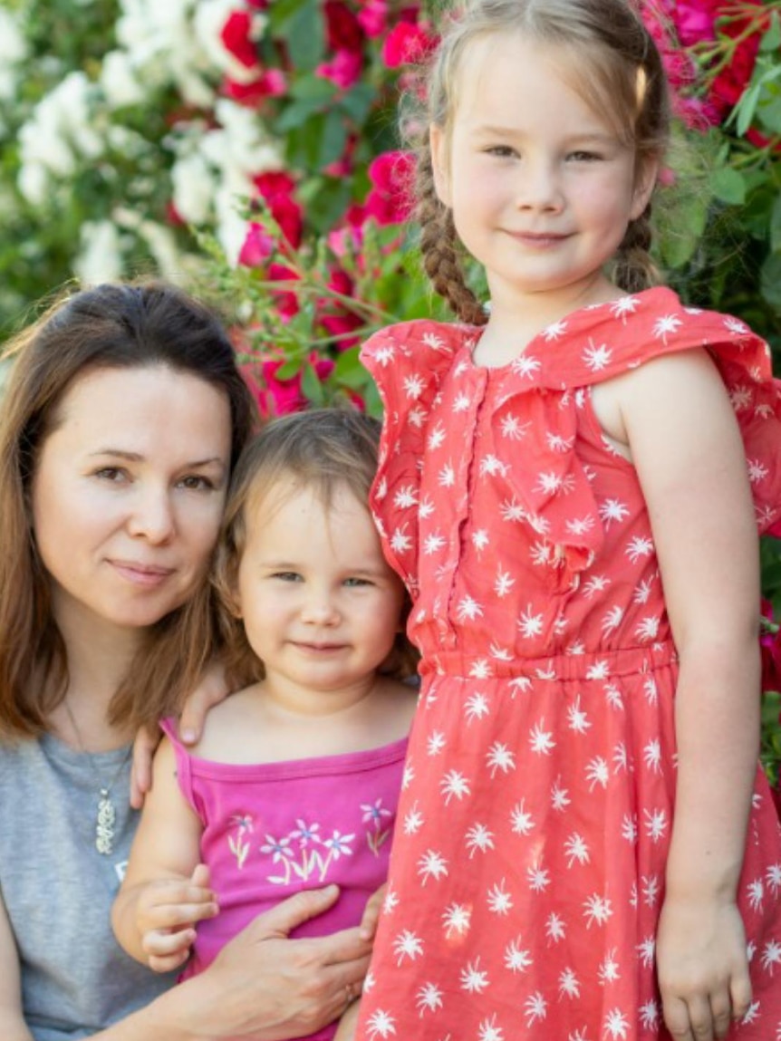 A woman crouches down next to two small girls.