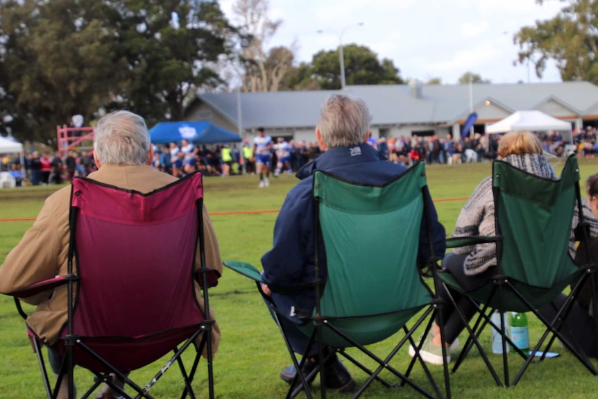 A rear view of rugby union spectators sitting on chairs on the sidelines at Charles Court Reserve in Nedlands.