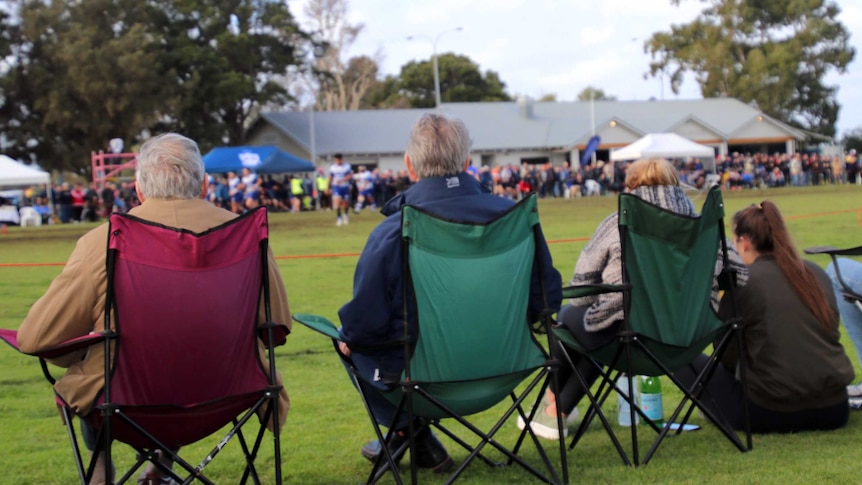 A rear view of rugby union spectators sitting on chairs on the sidelines at Charles Court Reserve in Nedlands.