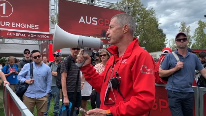 An official uses a megaphone to make an announcement to the crowd at the gates to the track.