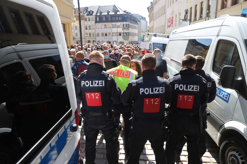 police stand in between police vehicles as people gather in the streets