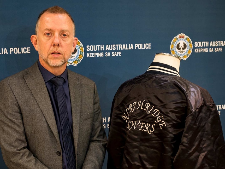 A man in a suit standing along side a black bomber jacket on a stand.