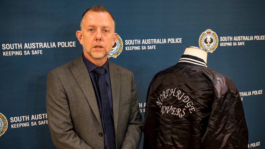 A man in a suit standing along side a black bomber jacket on a stand.