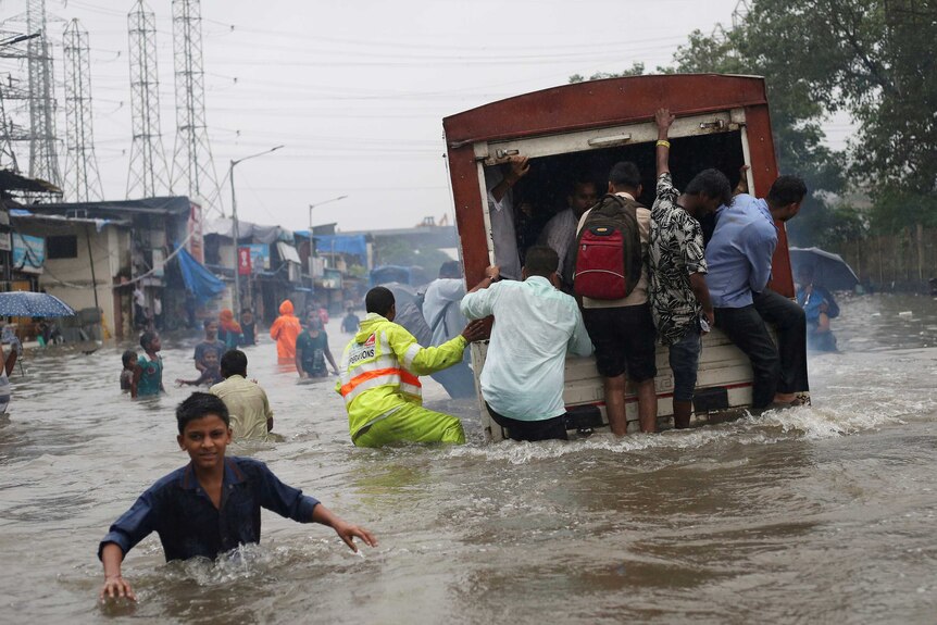 A group of people ride on the back of a truck in floodwaters in India