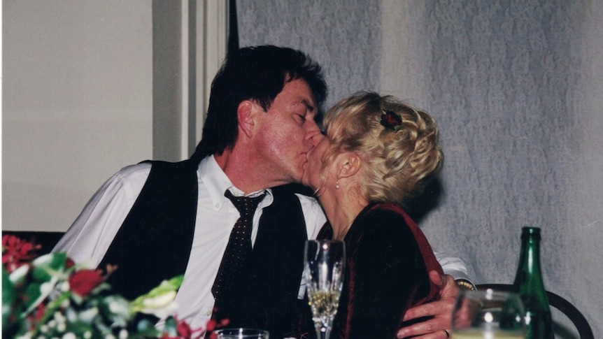 Terence and Christine Hodson kissing while seated at a table.