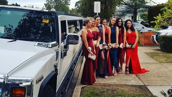 Seven young women in formal wear pose for a picture in front of a stretch Hummer limousine.