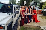 Seven young women in formal wear pose for a picture in front of a stretch Hummer limousine.